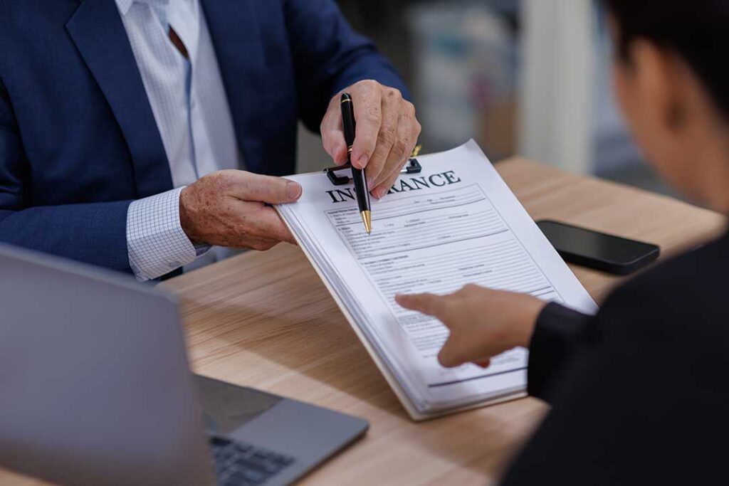 A close-up view of a hand holding insurance documents and a calendar with key dates marked.